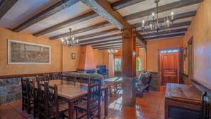 Un comedor con una gran mesa de madera y sillas, una lámpara de araña y una pared de piedra.