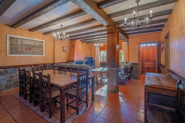 A dining area with a large wooden table and chairs, a chandelier, and a stone wall.