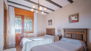 Un dormitorio con dos camas, cabecero de madera, mesita de noche, lámpara y ventana con cortinas.