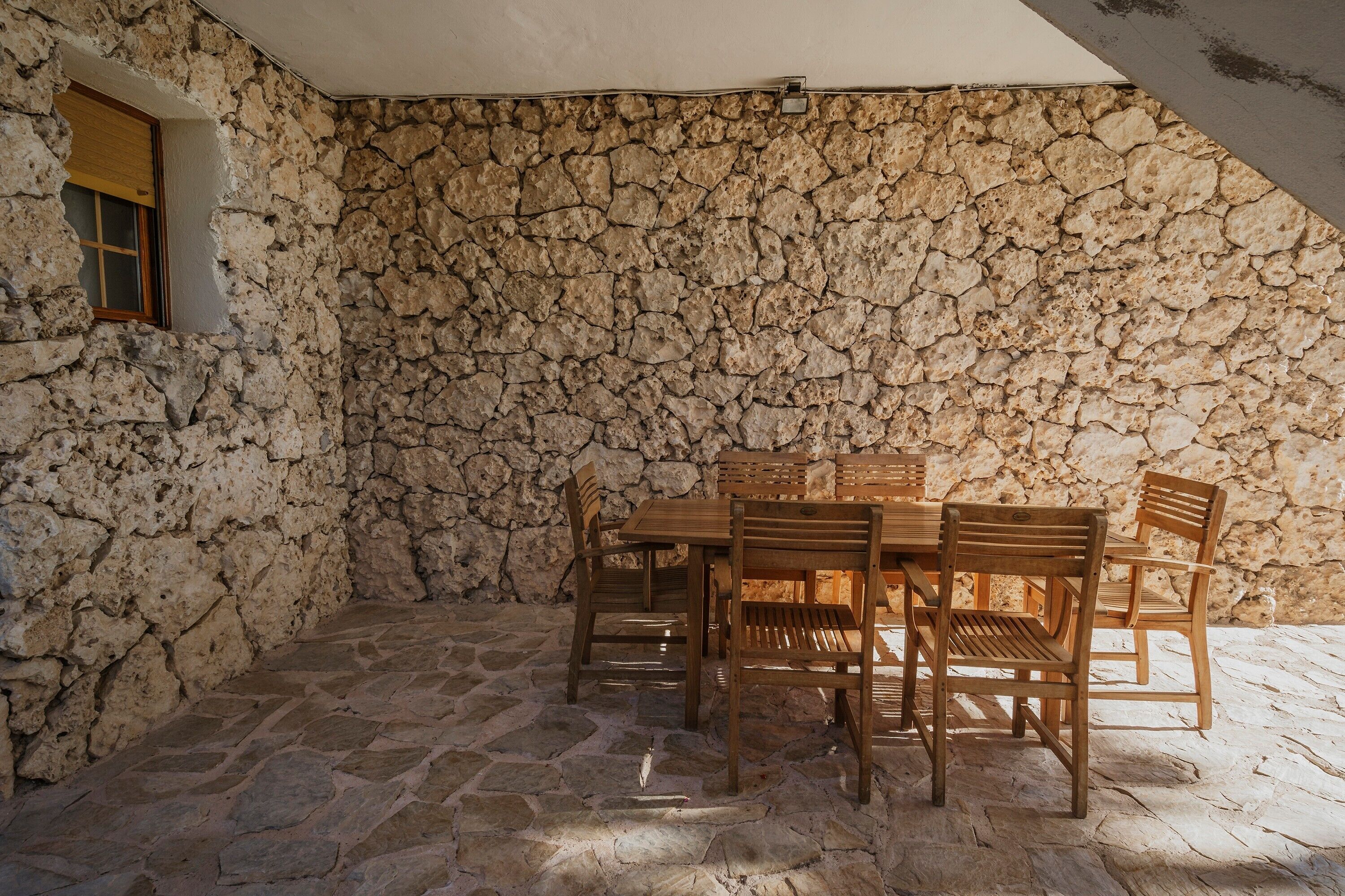 Una habitación con paredes de piedra, una mesa, sillas, un ventanal y una lámpara en el techo.