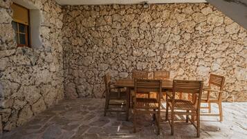 Una habitación con paredes de piedra, una mesa, sillas, un ventanal y una lámpara en el techo.