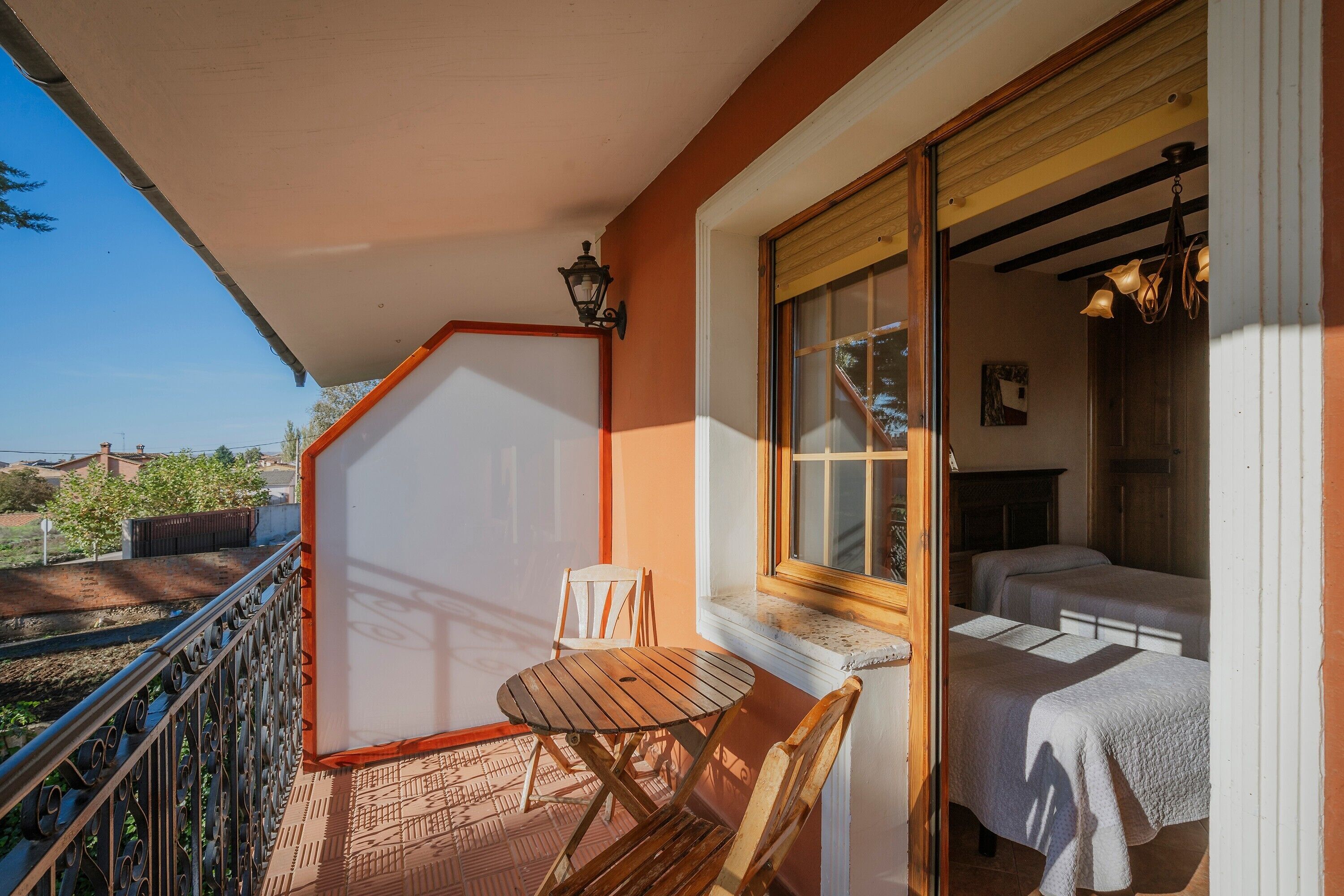 A balcony with a table and chairs, a window with curtains, and a bed with a headboard.