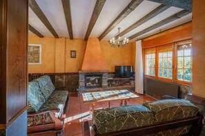 A cozy living room with a fireplace, wooden beams, a sofa, and a television.