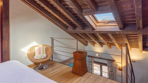 A room with a sloped ceiling, a wicker chair with a cushion, a bedside table, and a small wooden cabinet. - Apartment 'Alojamiento Taurus' with Balcony and Wi-Fi (Braojos de la Sierra)