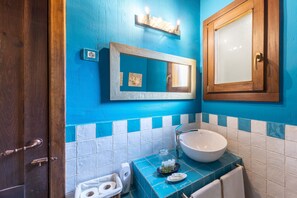 Ein Badezimmer mit Holztür, blauen Fliesen, einem weißen Waschbecken und einem Spiegel mit Holzrahmen.