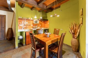 Un comedor con una mesa y sillas de madera, un microondas y una estantería con utensilios de cocina.