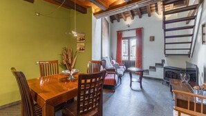 A dining area with a wooden table and chairs, a sofa, a fireplace, and a staircase. - Country House 'Alojamiento Perseus' with Mountain View, Balcony and Wi-Fi (Braojos de la Sierra)