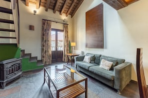 Una sala de estar con un sofá verde, una mesa de centro de madera, una mesa con cubierta de vidrio, una chimenea y una escalera.