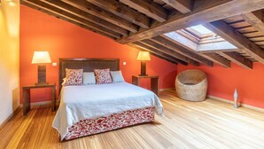 A bedroom with a wooden ceiling, a bed with a patterned bedspread, two bedside lamps, and a wicker chair. - Country House 'Alojamiento Hercules' with Mountain View, Balcony and Wi-Fi (BRAOJOS)