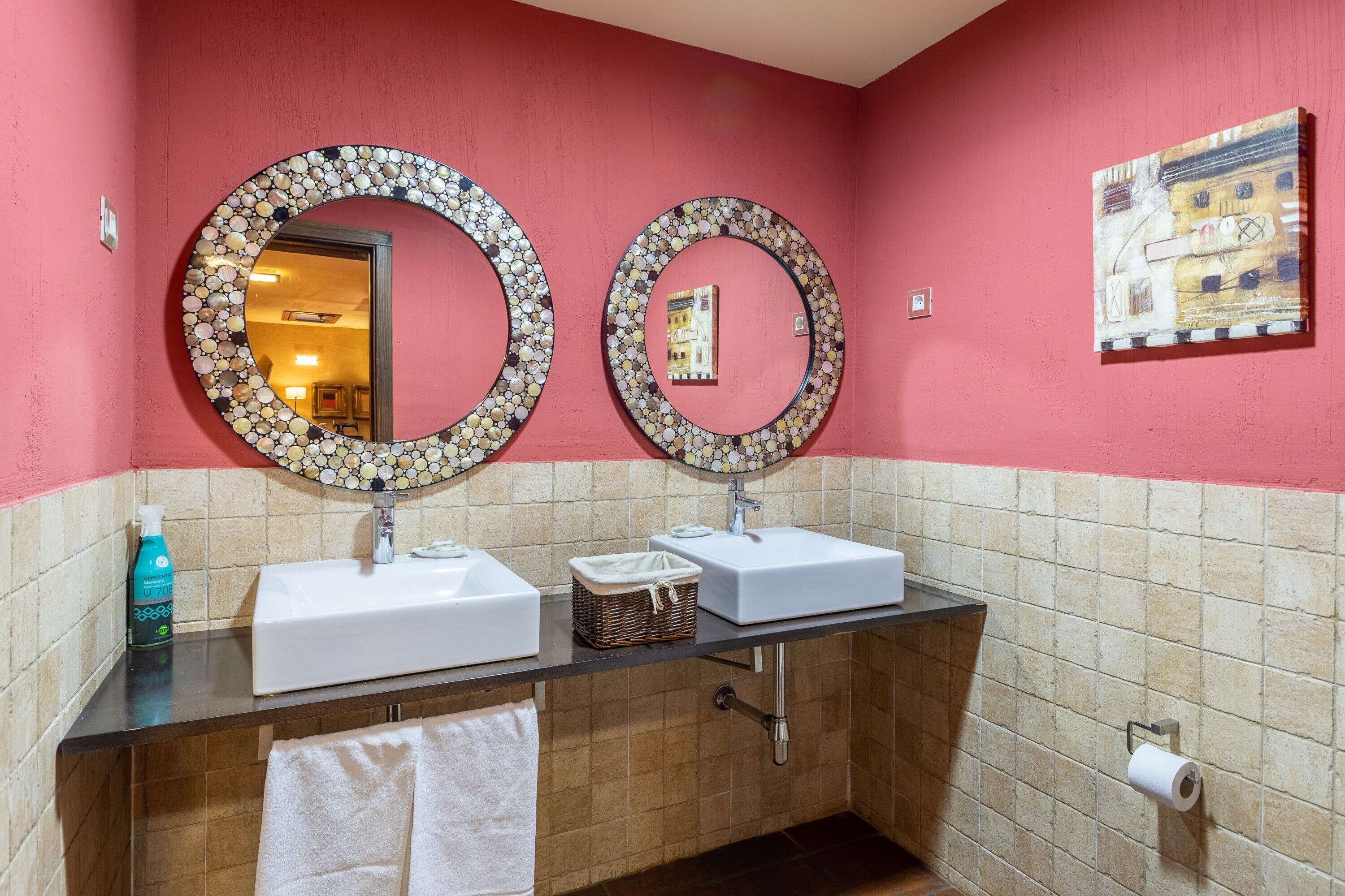 Een badkamer met twee wasbakken, een spiegel, een handdoekrek, een toiletrolhouder en een schilderij aan de muur.