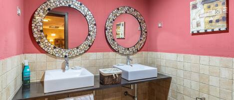 A bathroom with two sinks, a mirror, a towel rack, a toilet paper holder, and a painting on the wall.