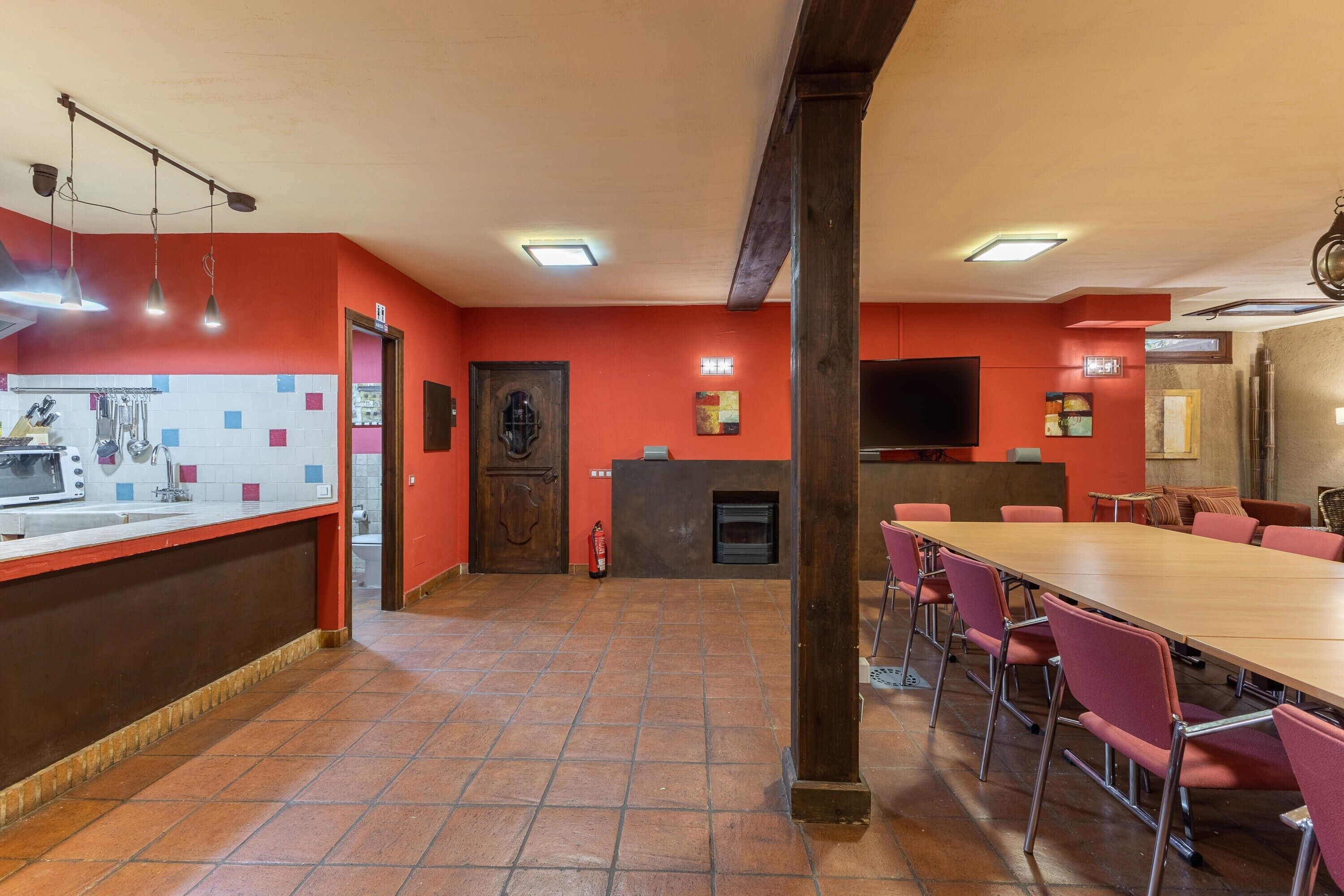 Een restaurant met een lange houten tafel, rode wanden en een betegelde vloer.