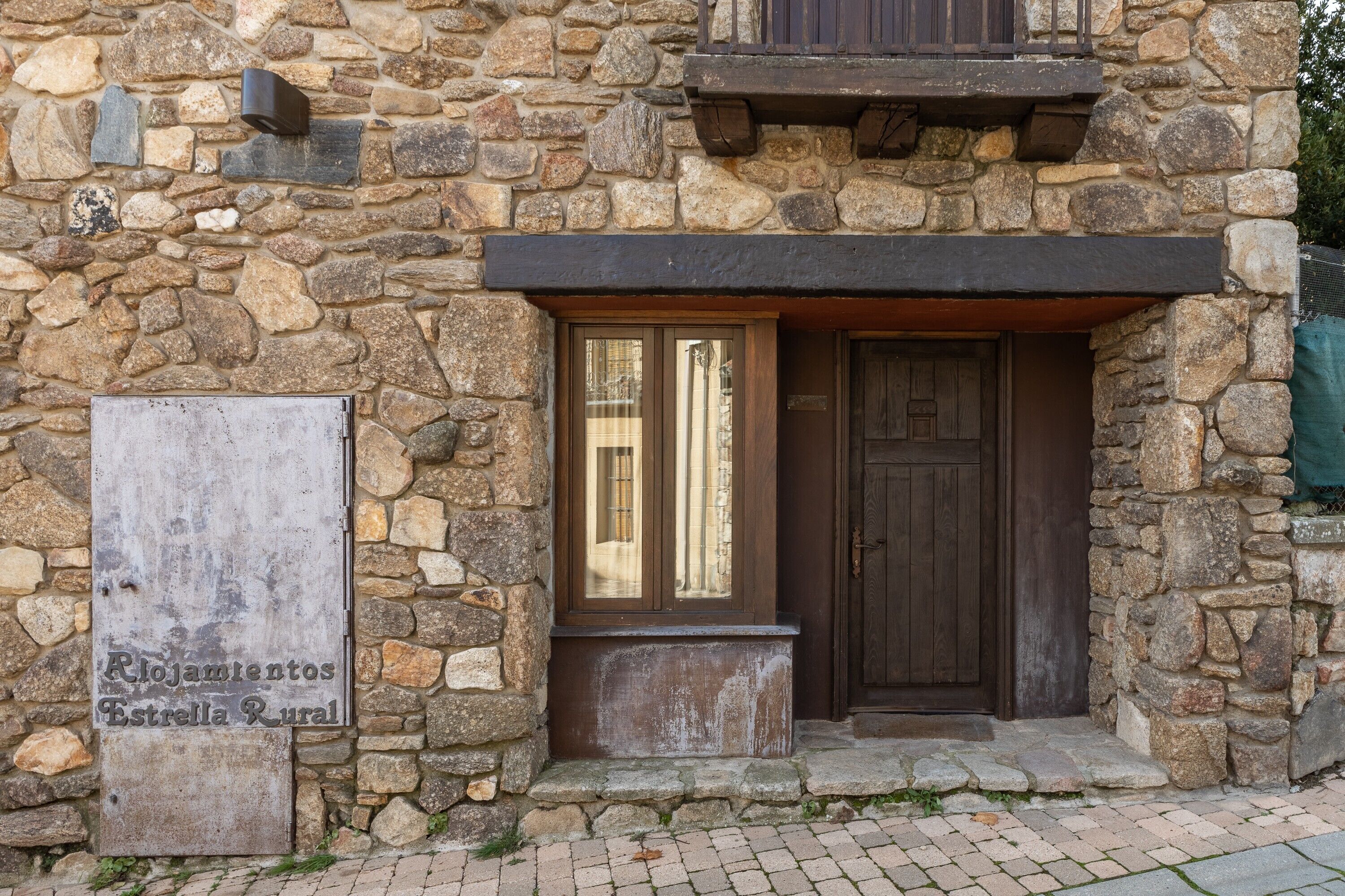 A stone building with a wooden door and window, a balcony, and a sign reading 'Rojamentos Estrella Rural'.