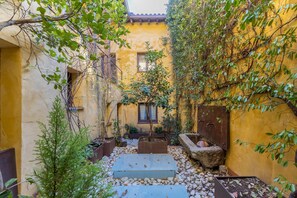 Ein Innenhof mit Baum, einem kleinen Garten und einem Gebäude mit gelben Wänden.