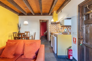A cozy living room with a sofa and a dining table, a kitchen with a tiled backsplash, and a fire extinguisher on the wall. - Country House 'Alojamiento Andromeda' with Mountain View and Wi-Fi (Braojos de la Sierra)