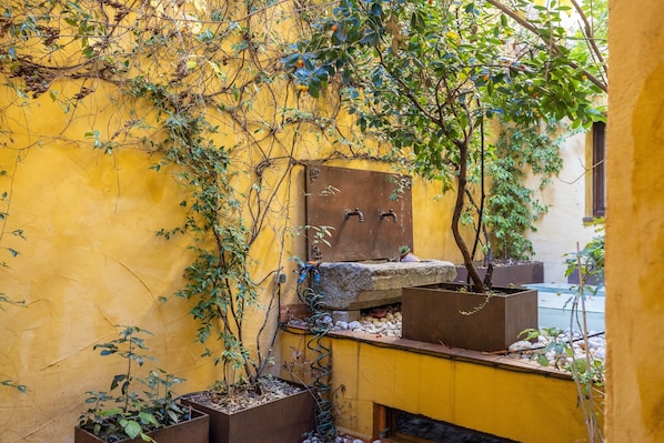 A narrow alley with yellow walls, a rustic stone bench, and potted plants.