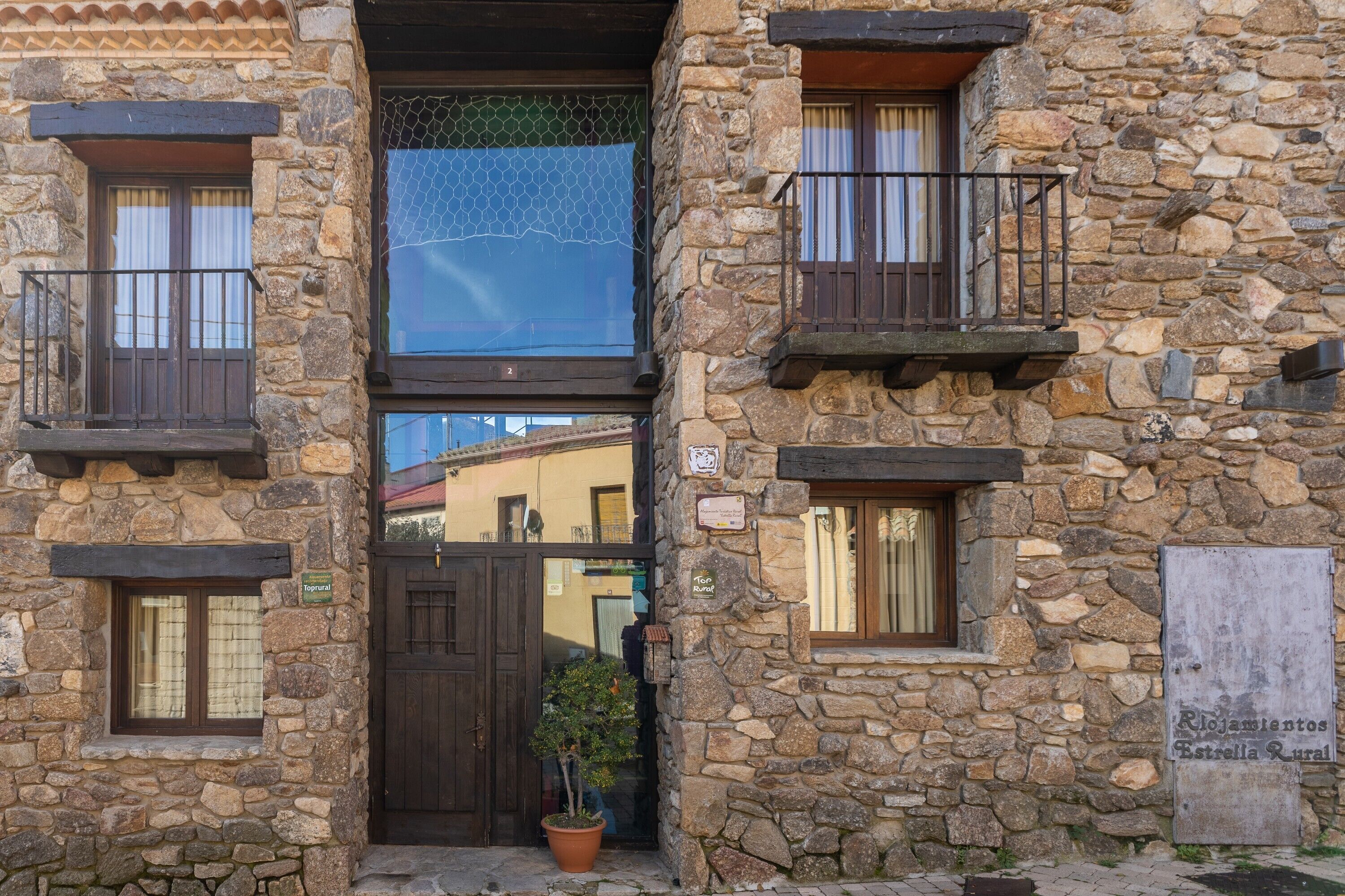Un bâtiment en pierre avec une porte en bois, des plantes en pot et un balcon.
