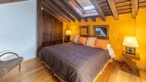 A bedroom with a wooden ceiling, a bed with a brown bedspread, two bedside lamps, a chair, and a mirror on the wall. - Country House 'Alojamiento Pegasus' with Mountain View, Balcony and Wi-Fi (Braojos de la Sierra)