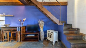 A room with a wooden staircase, a television, a vase with dried plants, and a vintage stove. - Country House 'Alojamiento Pegasus' with Mountain View, Balcony and Wi-Fi (Braojos de la Sierra)