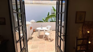 An open doorway leading to a terrace with a table and chairs, a potted plant, and a view of the sky.