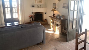A cozy living room with a fireplace, a sofa, a wooden cabinet with books, and a door with glass panels.