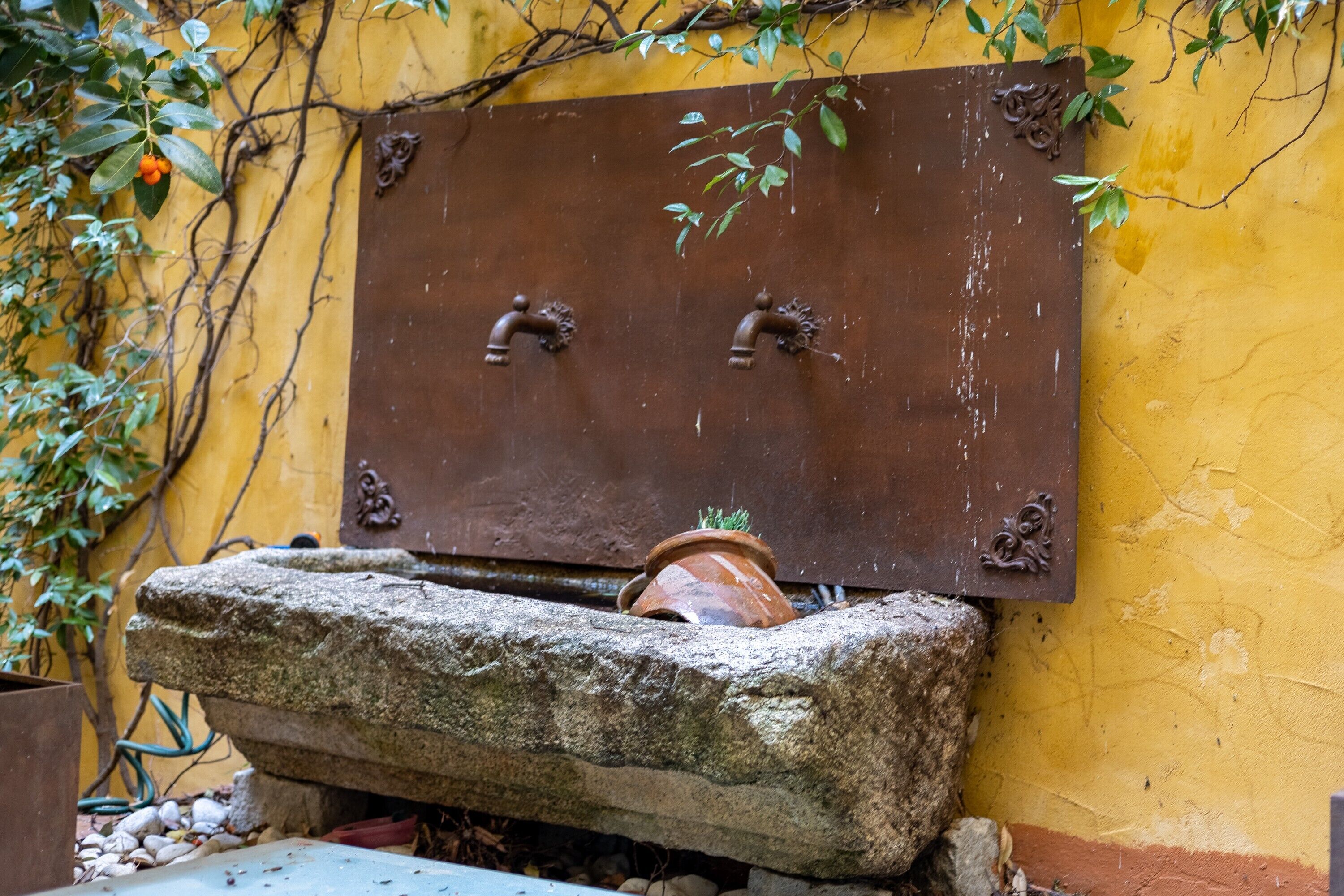 Ein rustikales Wasserspiel im Freien mit einem Steinbecken und einer Metallplakette.