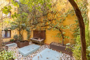 A courtyard with a yellow wall, a tree, and a bench.
