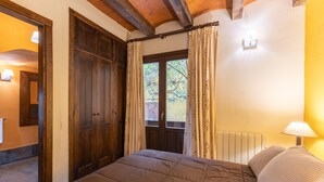 A bedroom with a bed, wooden door, window with curtains, and a lamp.