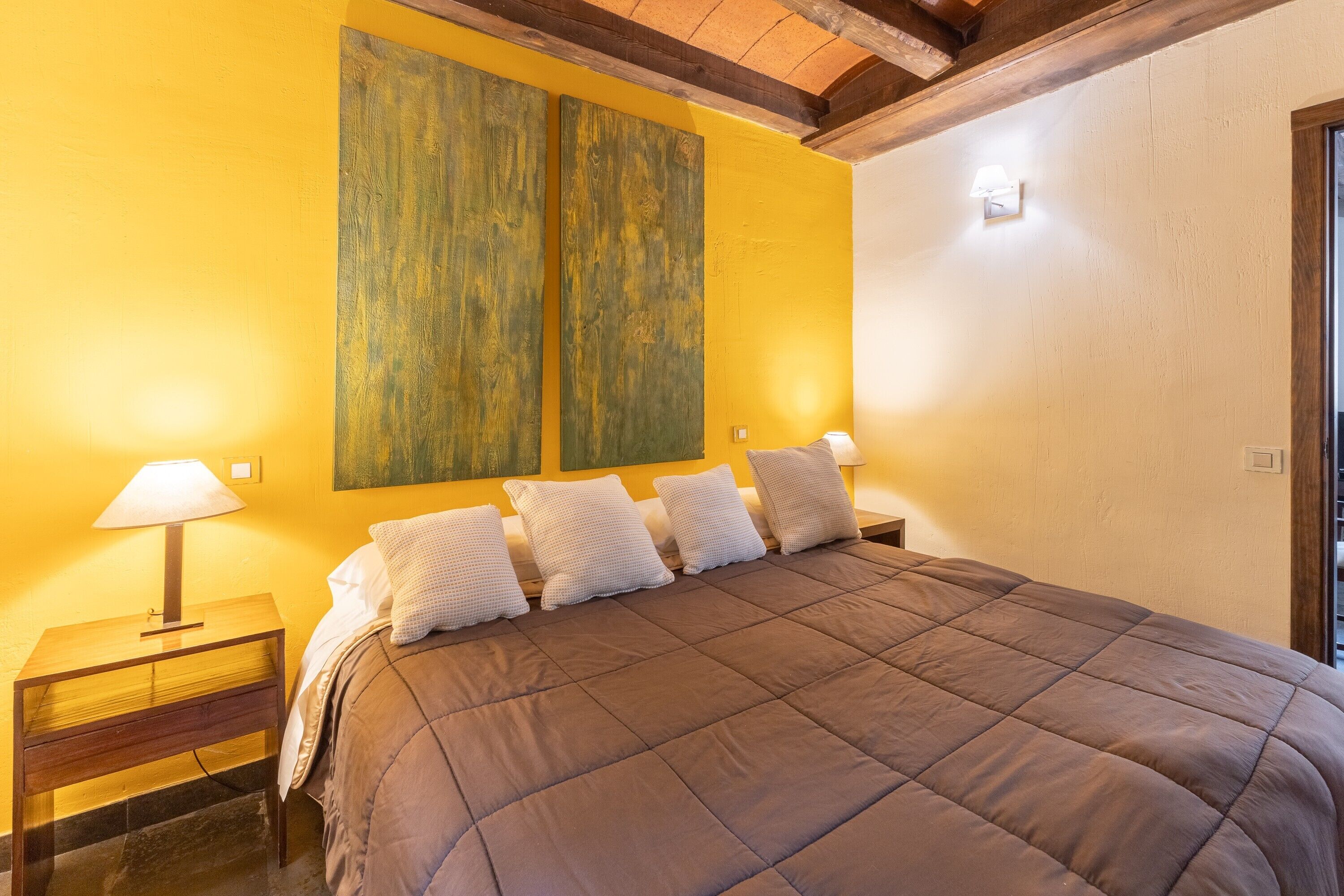 Een slaapkamer met een groot bed, twee bedlampen, een houten hoofdeinde en een gele wand.