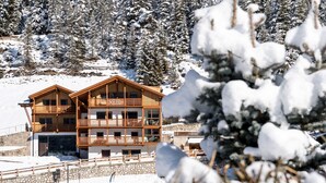 A multi-story wooden building with balconies, surrounded by snow-covered trees and a stone wall. - Apartment 'Villa Solinda App Vivaldi' with Mountain View, Private Terrace and Wi-Fi (Selva)