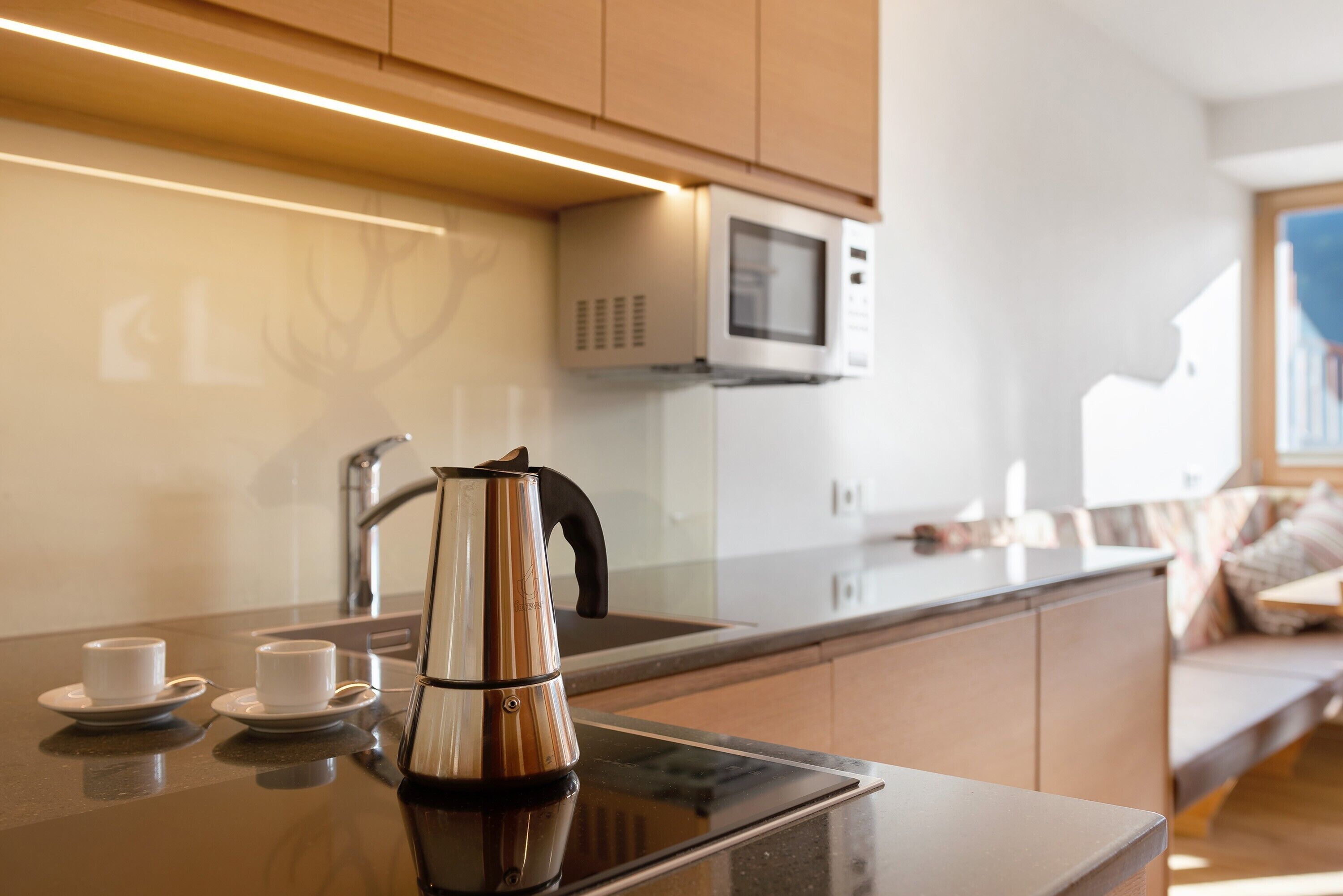 Una cucina moderna con bollitore, due tazze, forno a microonde e lavandino.