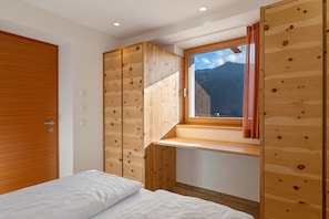 Une chambre avec une armoire en bois, un lit et une fenêtre donnant sur la montagne.