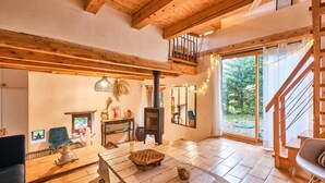 A spacious living area with a wooden ceiling, a fireplace, a dining table, and a view of the outdoors. - Holiday Home 'L'atelier M' with Mountain View, Private Terrace and Garden (Quaix-en-Chartreuse)