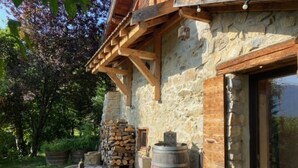 A rustic stone building with a wooden porch, a fire pit, and a barrel. - Holiday Home 'L'atelier M' with Mountain View, Private Terrace and Garden (Quaix-en-Chartreuse)