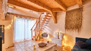 A cozy room with a wooden staircase, a woven wall hanging, a blue sofa, and a coffee table with a chessboard. - Holiday Home 'L'atelier M' with Mountain View, Private Terrace and Garden (Quaix-en-Chartreuse)