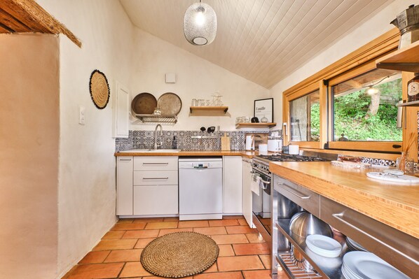 A kitchen with white cabinets, a dishwasher, an oven, and a window with a view of greenery. - Holiday Home 'L'atelier M' with Mountain View, Private Terrace and Garden (Quaix-en-Chartreuse)