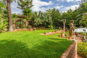 Un jardin luxuriant agrémenté d’une statue, d’un bâtiment en briques et d’une grande variété de plantes.