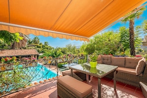 Une terrasse avec une piscine, du mobilier d’extérieur et une vue sur une maison et la verdure.