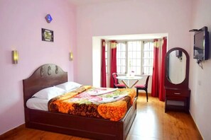A bedroom with a bed, a desk, a chair, a mirror, and a television. - Green Park Gran Inn (Kodaikanal)