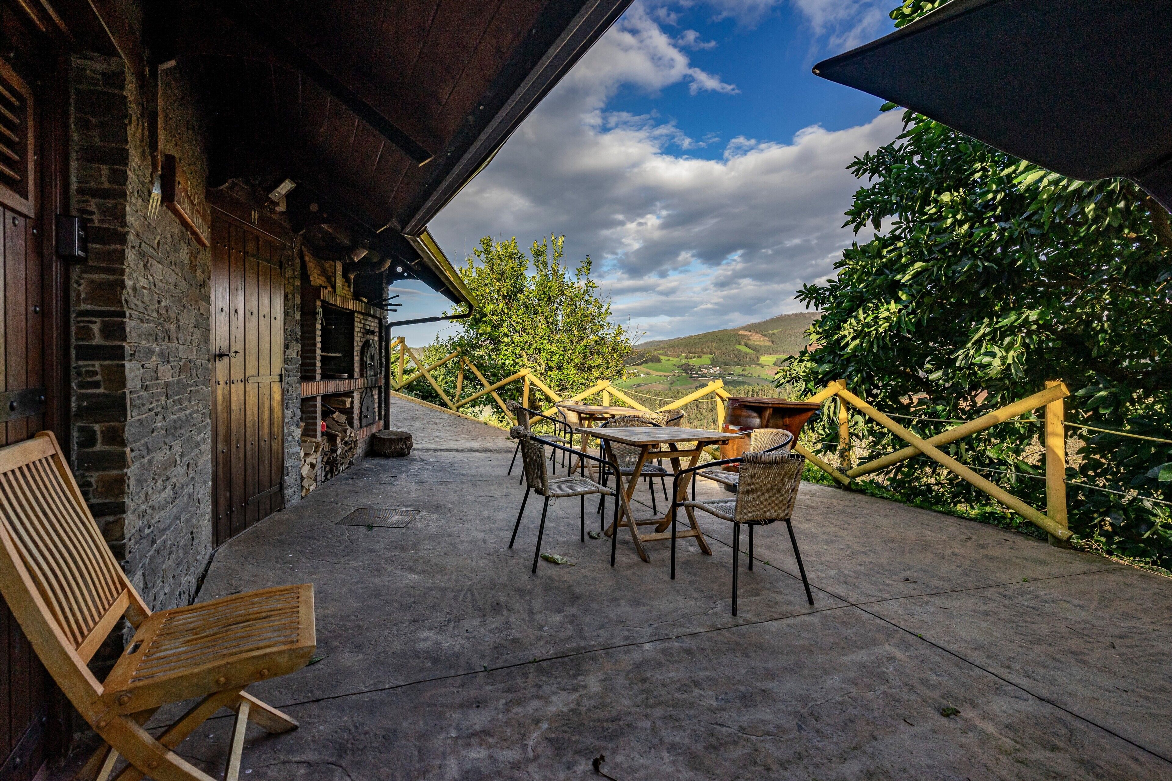 Eine Terrasse mit Holzmöbeln, einer Steinmauer und Blick auf die Landschaft.