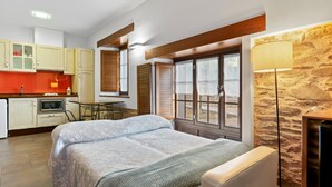 A bedroom with a bed, a bedside table, a lamp, a window with a view, and a kitchenette with cabinets and a microwave.