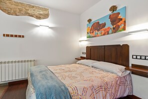 A bedroom with a bed, a radiator, a wooden headboard, a wall-mounted light, and a painting of flowers.