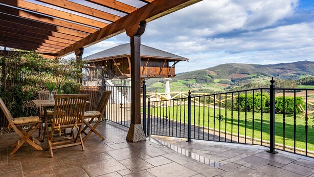 Une terrasse couverte avec une table et des chaises en bois, une vue sur la campagne et un espace clos.