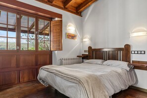 A bedroom with a wooden headboard, a large window with blinds, a radiator, and a wall-mounted shelf.