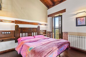 Un dormitorio con cabecera de madera, cama con ropa de cama rosa, pared de piedra, ventana y radiador.