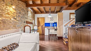 Ein modernes Interieur mit einer Steinwand, Holzbalkendecke, einem weißen Sofa, einer Küchenzeile und einem Fernseher.