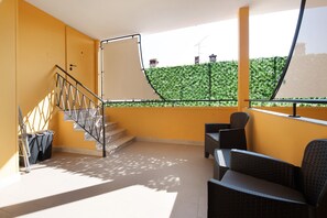 Un balcon doté d’un escalier, d’un espace salon extérieur et offrant une vue sur une haie verdoyante.