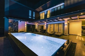 Un espace piscine extérieur moderne, doté d’une structure en verre, de sièges et d’un intérieur bien éclairé.