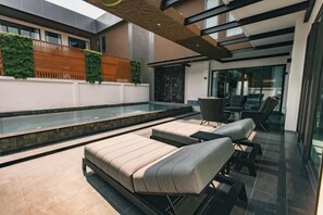 A modern outdoor pool area with lounge chairs and a glass-enclosed patio. - Astro Luxury: 4-6 beds Ultra Luxury Pool Villa with Daily Cleaning (Pattaya)