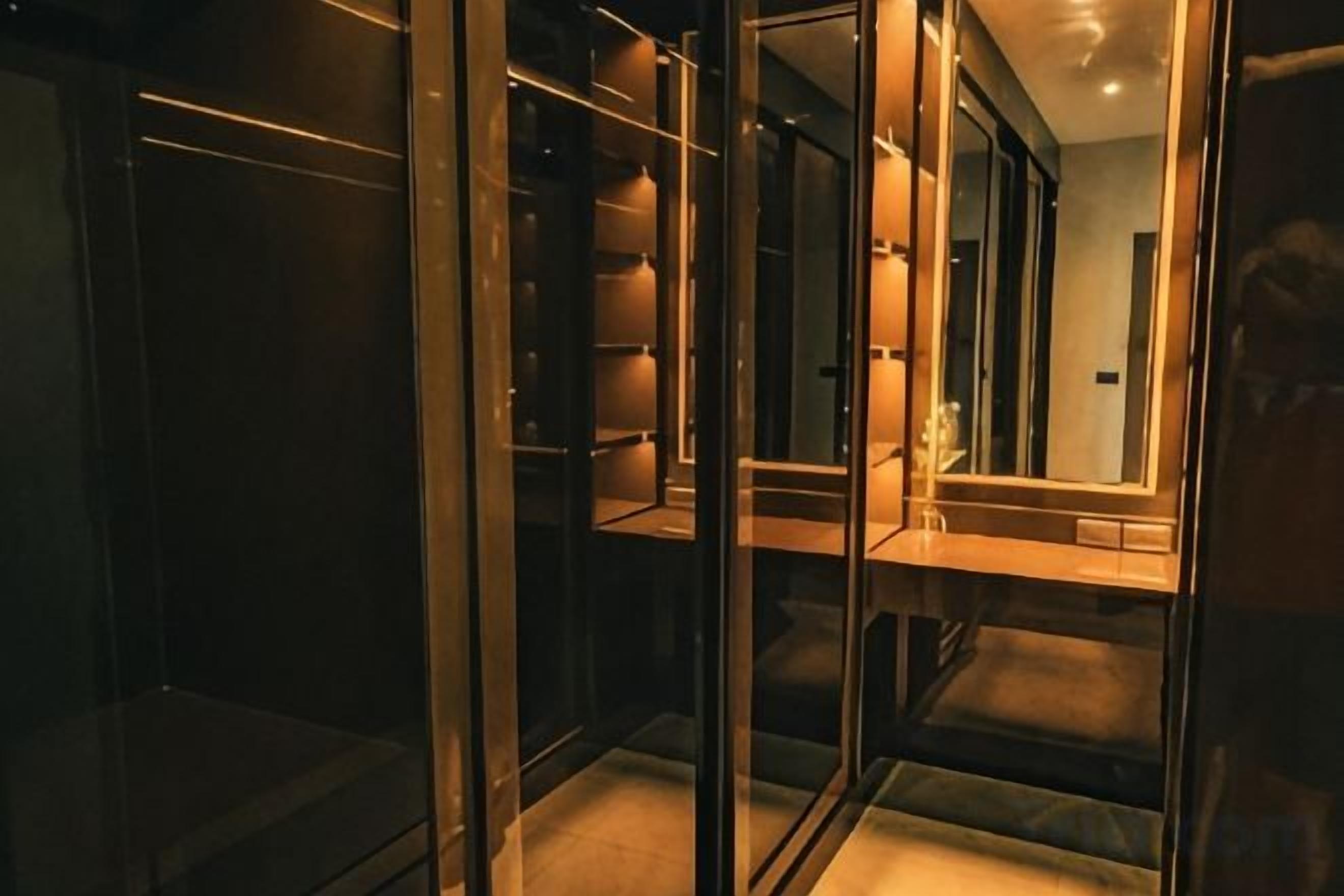A glass-walled elevator with a mirrored interior, reflecting a hallway with a door and a light fixture.